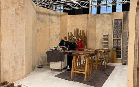 ifs-Studierende stehen beim Studiobau neben bemalten Holzpaletten