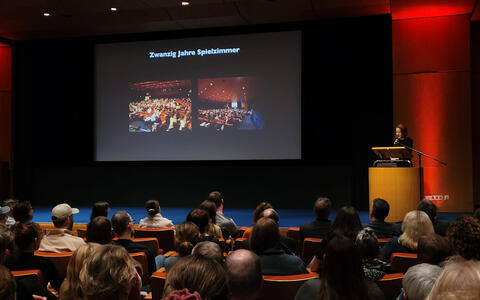 Eine Frau steht vor einem gefüllten Kinosaal am Mikrofon