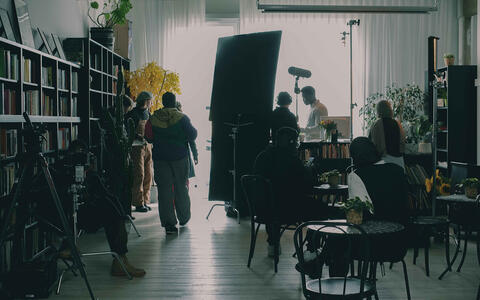 Ein Filmteam in einem großen Raum mit Bücherregalen und kleinen Tischen mit Stühlen.