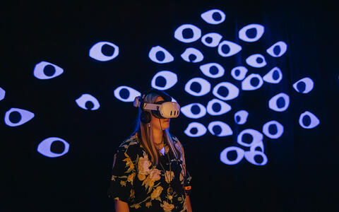Eine Frau steht in einem dunklen Raum mit VR-Brille auf dem Kopf
