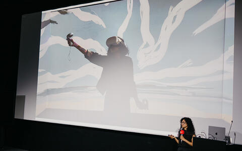 Keynote von Naima Karim auf der Bühne vor der Kinoleinwand