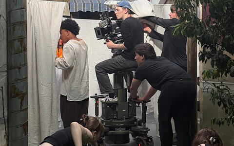 Studierende filmen zwischen weißen Tüchern auf einer Wäscheleine hindurch. Zwei Studentinnen verdecken den grünen Boden mit einem schwarzen Tuch