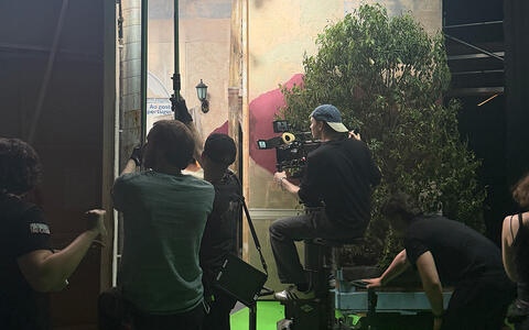 Studierende filmen eine Szene am Set. Rechts steht eine Pflanze. Der Boden ist grün