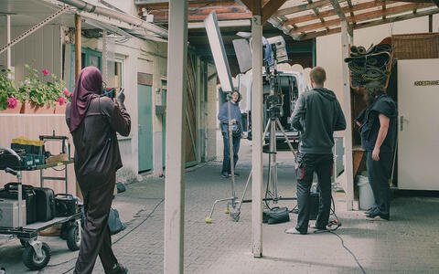 Ein Filmteam in einem Hinterhof. Im Hintergrund steht ein weißer Transporter mit geöffneten hinteren Türen.