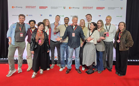 Gruppenfoto von Studierenden mit Steven Kane auf einem roten Teppich vor einer Werbewand
