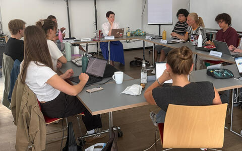 Eine Gruppe sitzt an Tischen in einem Seminarraum