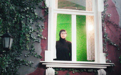 Eine ganz in schwarz gekleidete Frau steht hinter einem Fenster