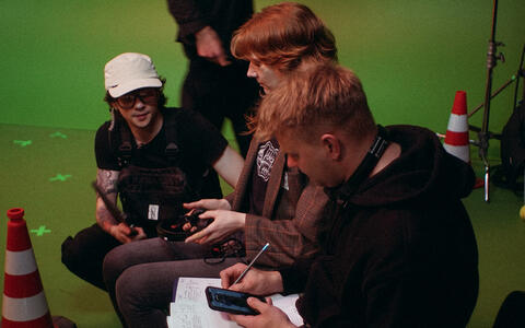 Drei Studierende sitzen vor einem Green Screen