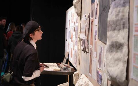 Eine junge Frau mit schwarzer Mütze schaut sich Ausstellungsstücke auf einer Wand an