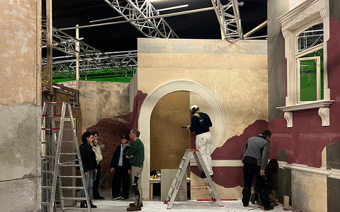 Studierende arbeiten im Studio an der Fassade eines alten Art-Deco-Hauses. Eine andere Gruppe Studierende ist im Gespräch mit dem Studioleiter