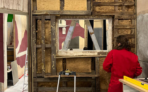 Eine Studentin arbeitet an einer offenen Wand. Man sieht das Dämmmaterial und Holzlatten.