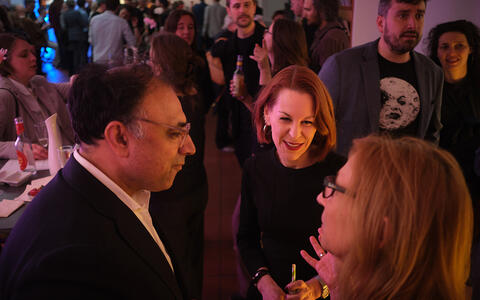 Zwei Frauen und ein Mann im Gespräch. Im Hintergrund viele Menschen im Gespräch