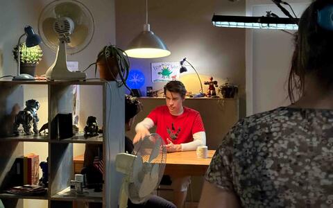 Zwei junge Männer sitzen in einer Wohnung an einem Tisch, über ihnen hängt eine Tonangel.