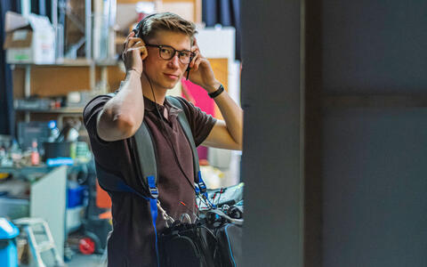 Am Set von »Dünn ist die Haut« im ifs-Studio: Ein Student verantwortet den Ton und fasst sich mit beiden Händen an das Headset.