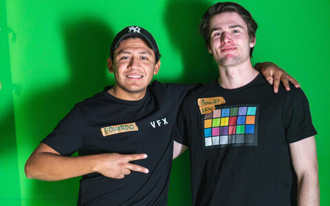 Am Set von »Knallrot« im ifs-Studio stehen zwei Studenten vor einer grünen Wand und lächeln in die Kamera