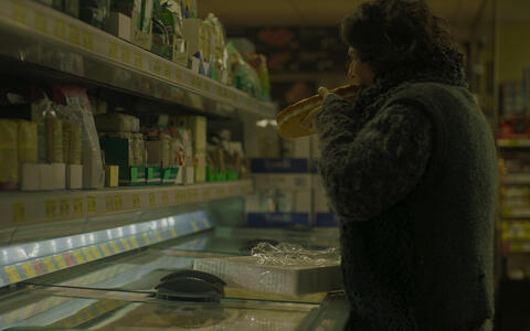 Eine Frau steht im Supermarkt vor den Tiefkühltruhen und beißt in einen Tiefkühlkuchen