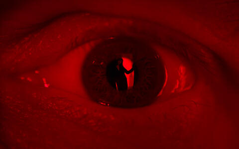 Ein Auge in rotem Licht, in dem die Siliouette einer Frau zu sehen ist.