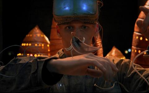 Ein animiertes Filmstandbild. Ein junger Mann steht in schützender Laborausrüstung. Er untersucht eine Kakerlake auf seiner Hand.