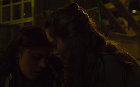 Zwei junge Frauen sitzen Stirn an Stirn draußen im Dunklen