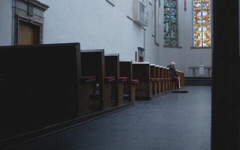 Blick in eine Kirche. Ein älterer Mann sitzt auf einer Kirchenbank und hält einen Besen in der Hand