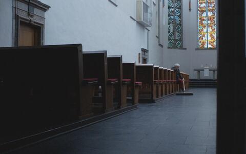 Blick in eine Kirche. Ein älterer Mann sitzt auf einer Kirchenbank und hat einen Besen in der Hand